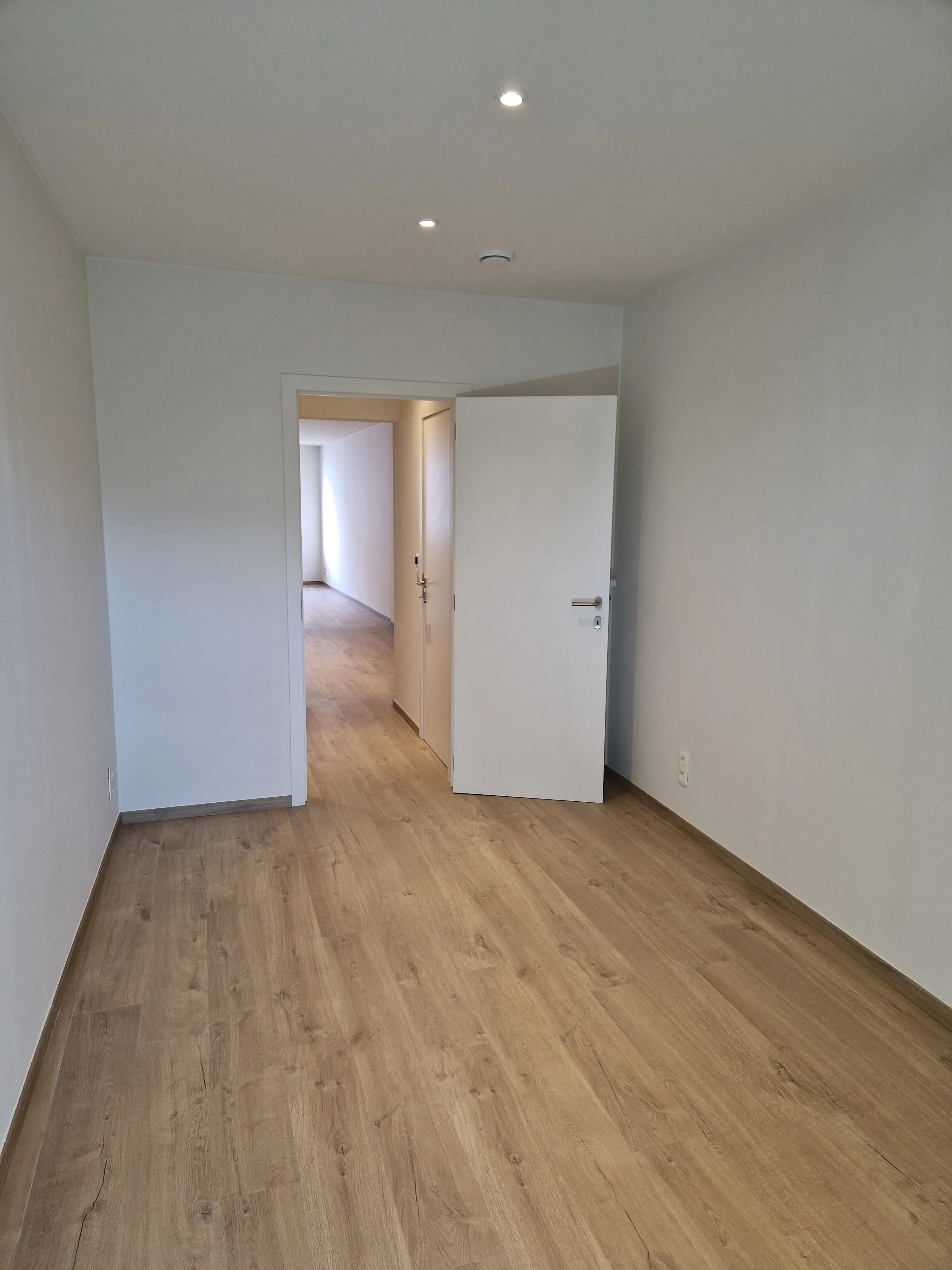 Slaapkamer met warme houten vloer en witte deur te huur